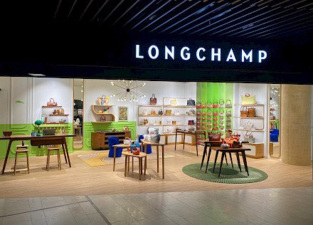 Heller Eingangsbereich des Longchamp Stores in München mit geschwungener Holztreppe und Schaufensterpuppe